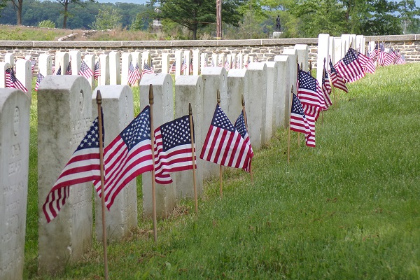 White marble headstones adorned with small American flags in the Gettysburg National Cemetery